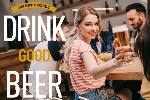 スマートな人の近くで軽いビールを飲みながらカメラを見ながら笑顔の若い女性の選択的な焦点は良いビールイラストを飲む - 写真・画像