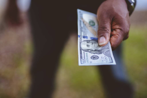 Closeup shot of a person holding a hundred dollar bill with a blurred background - concept bribing - Foto, Bild