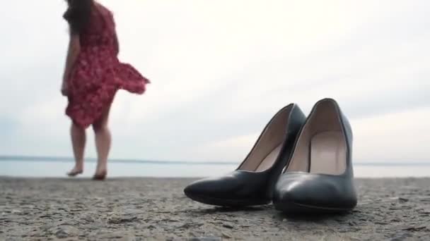 slank meisje in korte rode jurk met lang haar gooit donkergroene schoenen op de stenen pier en loopt gelukkig naar zee. Genieten van de vrijheid. vakantie zomerdag op de pier van de zee. Ver van de stad - Video