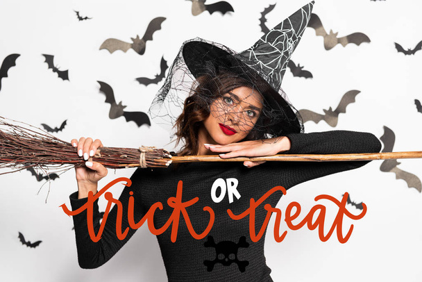 attraente donna in cappello strega tenere scopa ad Halloween vicino trucco o trattare lettering
 - Foto, immagini
