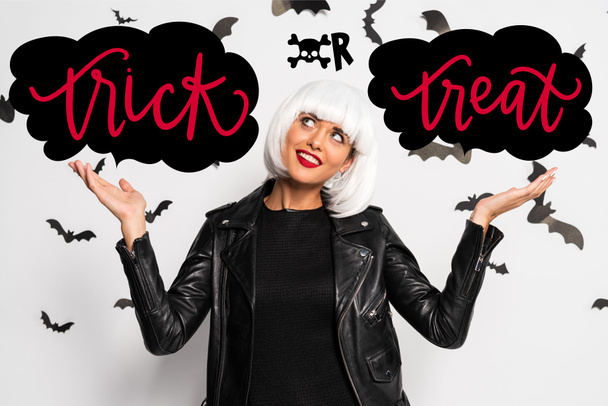 attractive woman in white wig pointing with hands at clouds near trick or treat lettering - Photo, Image