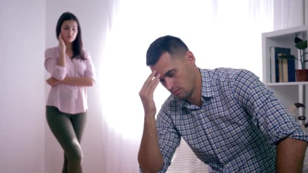 Familienstreit, verärgerter Mann nach Streit mit Frau, die zu Hause sitzt, faltet Hände in Gesichtsnähe und Frau im Stehen - Filmmaterial, Video