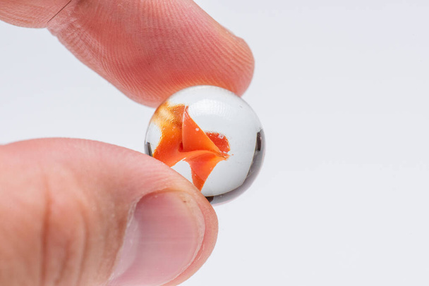 Mármol de cristal naranja sostenido por dos dedos
 - Foto, imagen