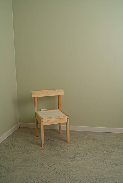 Одинокий детский стул в углу светлой зеленой комнаты
. - Фото, изображение