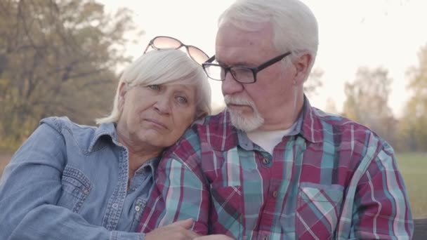Close-up of a Caucasian senior couple sitting on the bench and talking. Mature husband calming down his beautiful senior wife. Aging together, eternal love concept. - Video