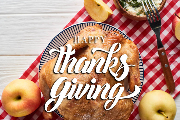 top view of roasted turkey with happy thanksgiving illustration, apples served on white wooden table with red plaid napkin - Foto, imagen