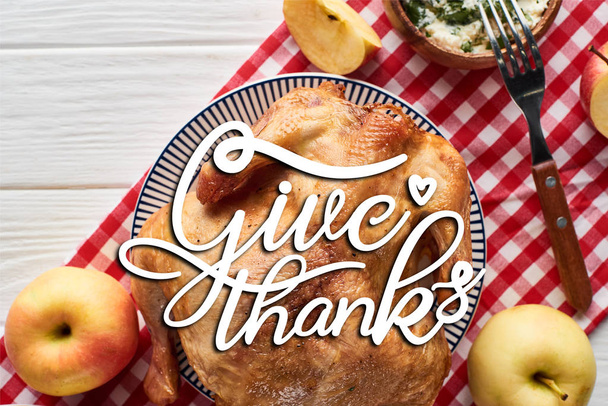 top view of roasted turkey with give thanks illustration, apples served on white wooden table with red plaid napkin - Photo, Image