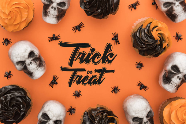 top view of delicious Halloween cupcakes with spiders and skulls on orange background with trick or treat illustration - Fotoğraf, Görsel