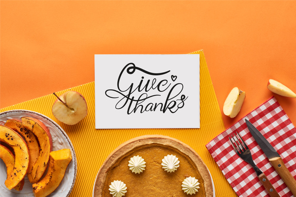 top view of delicious pumpkin pie near card with give thanks illustration on orange background with apples - Photo, Image