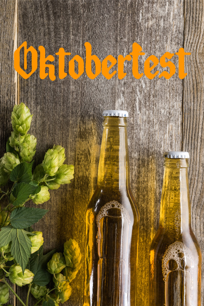 top view of fresh beer in bottles with green hop on wooden surface with Oktoberfest lettering - Photo, Image