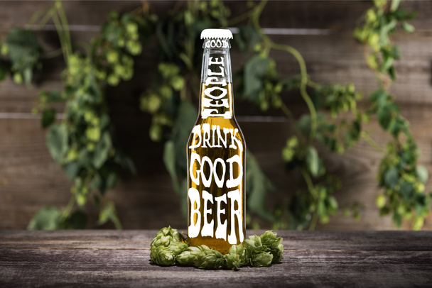 свіже пиво в пляшці з добрими людьми п'ють хороше пиво, що виливається біля зеленого хмелю на дерев'яній поверхні
 - Фото, зображення