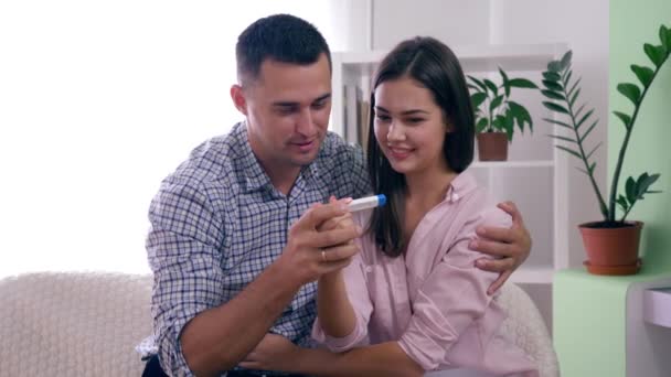 zdravý rodinný pár s těhotenským testem šťastný s pozitivním výsledkem a šťastně objímají jeden druhého v pokoji doma - Záběry, video