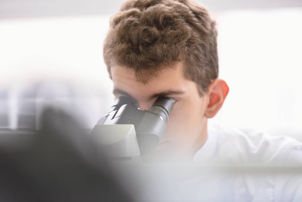 Young male scientist looking through a microscope in a laborator - Foto, Bild