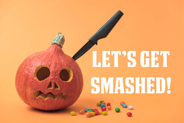 жуткая Хэллоуинская тыква с ножом и конфетками на оранжевом фоне с разбитыми иллюстрациями
 - Фото, изображение