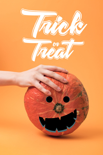 partial view of woman touching pumpkin on orange background with trick or treat illustration - Foto, Imagen