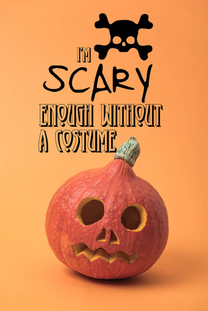 spooky carved Halloween pumpkin on orange background with i am scary enough without a costume illustration - Photo, Image