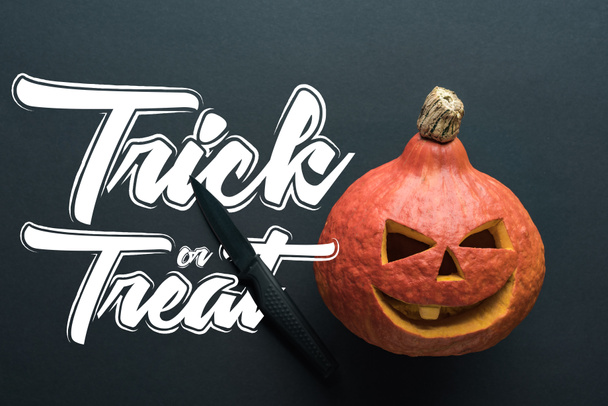 top view of carved spooky Halloween pumpkin with knife on black background with trick or treat illustration - Zdjęcie, obraz