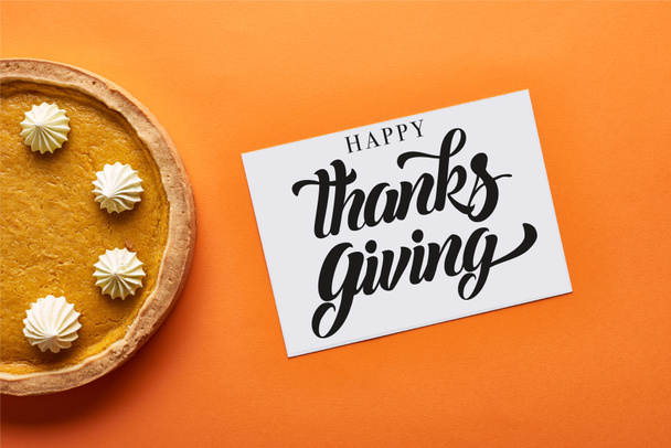 top view of pumpkin pie and card with happy thanksgiving illustration on orange background - Foto, Imagem