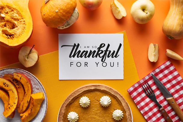 top view of pumpkin pie, ripe apples and card with i am so thankful for you illustration on orange background - Foto, Bild