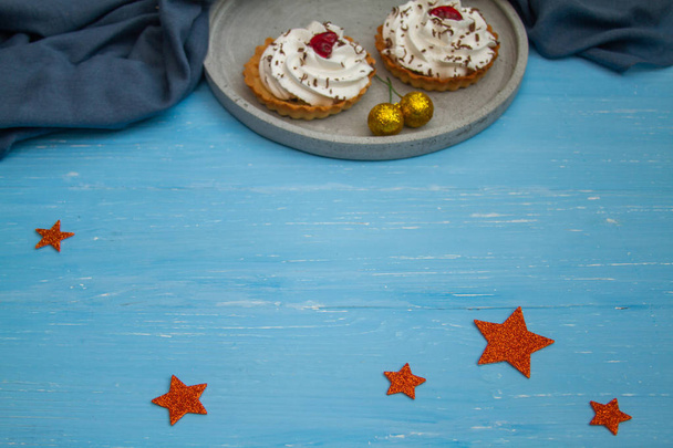 Mavi ahşap bir masada gri bir tabakta kremalı pasta. Kompozisyonun altında parlak dekoratif yıldızlar.  - Fotoğraf, Görsel