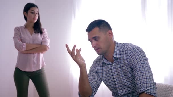 portrait of disappointed guy after quarrel with female sitting at home folding hands near face and woman standing - Footage, Video