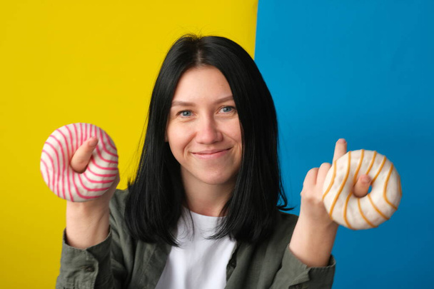 smiling girl holding donuts on blue and yellow background - Фото, зображення