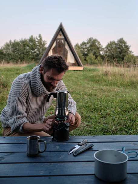 Young man making coffee in geyser coffee maker. Hipster in nature. Camping concept - Photo, Image