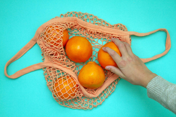 Una mano femenina toma una mandarina de una bolsa de compras. En la bolsa de hilo hay cítricos
. - Foto, imagen