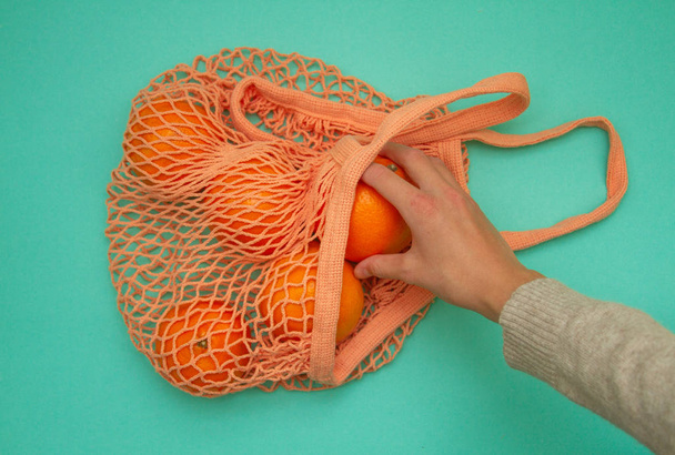 Una mano femenina toma una mandarina de una bolsa de compras. En la bolsa de hilo hay cítricos
. - Foto, Imagen