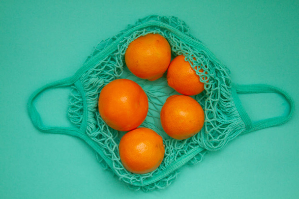 Tangerines in green mint color string bag on a turquoise background. Citrus in a wicker bag on paper. Shot from above. - Φωτογραφία, εικόνα