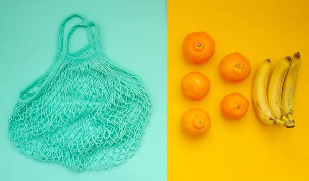 Мандарины и апельсины лежат в нео-мятной сумке. - Фото, изображение