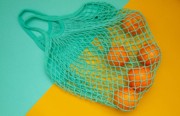 Mandarinas en una bolsa de hilo de color menta verde sobre un fondo turquesa. Cítricos en una bolsa de mimbre sobre papel. Disparo desde arriba.
. - Foto, Imagen