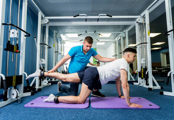 Rehabilitation therapy. Young man doing exercises on mat under supervision of physiotherapist. Treatment pain in spine - Foto, Bild