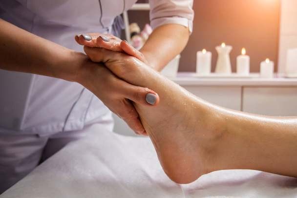 Beautiful young woman enjoying foot massage in spa salon. Cosmetology concept - 写真・画像