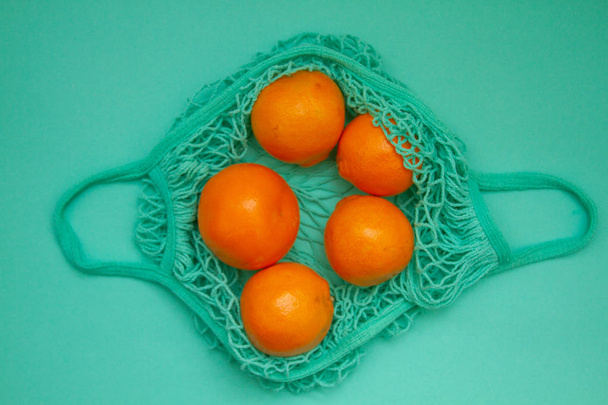 Tangerines in green mint color string bag on a turquoise background. Citrus in a wicker bag on paper. Shot from above. - Foto, Imagem