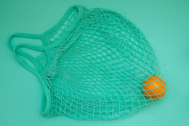 Mandarin in mint green string bag on a turquoise background. Citrus in a wicker bag on paper. Shot from above. - Foto, immagini