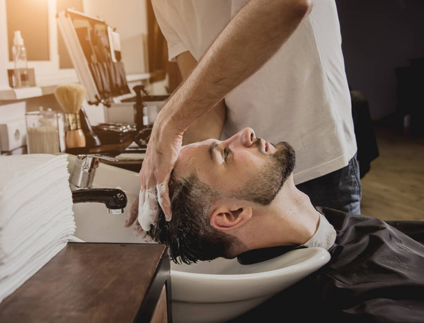 Young man with trendy haircut at barber shop. Barber washes customer head. Concept barbershop. - Φωτογραφία, εικόνα