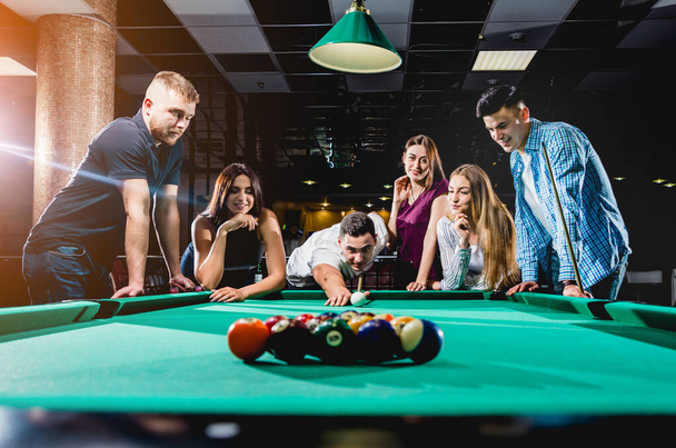 Group of young cheerful friends playing billiards. Funny time after work - Photo, image