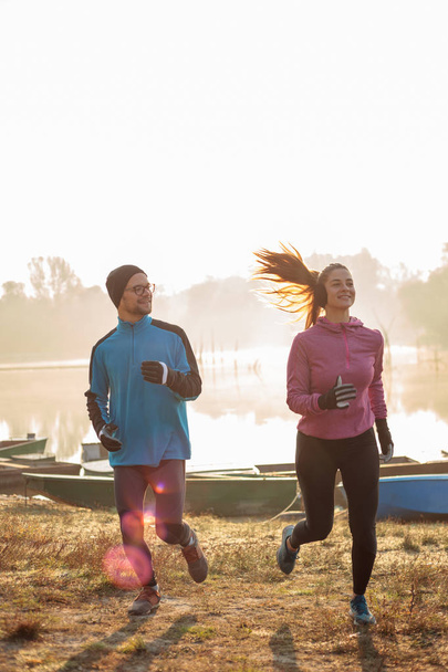 Χαμογελώντας ευτυχισμένο ζευγάρι τρέχει προς την κάμερα από το ποτάμι ή τη λίμνη νωρίς το πρωί - Φωτογραφία, εικόνα
