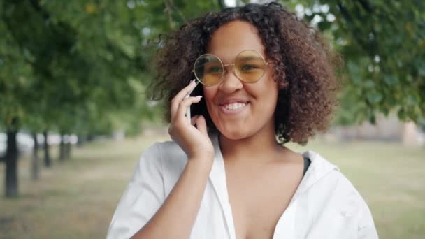 Excited African American woman speaking on mobile phone in city park laughing - Footage, Video