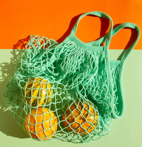 Małe dekoracyjne jesienne dynie w zielonej torbie strunowej. Warzywa w torbie na zakupy na zielonym tle. - Zdjęcie, obraz