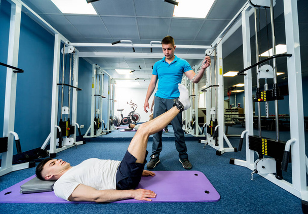 Rehabilitation therapy. Young man doing exercises on mat under supervision of physiotherapist. Treatment pain in spine - Zdjęcie, obraz