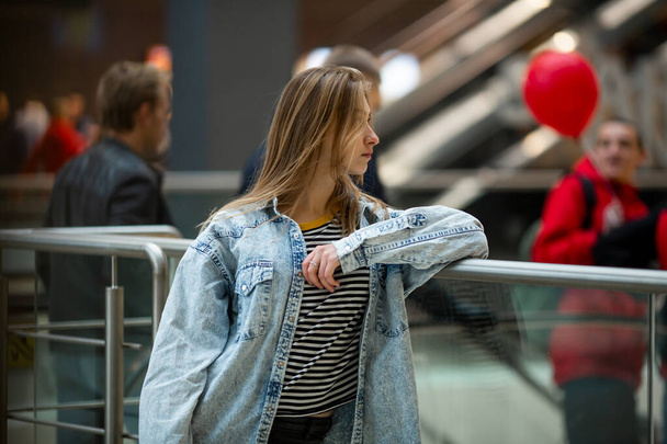 Teenager. Young pretty white caucasian teenage girl with long hair with problem skin and long hair in a shopping center near the railing. - Zdjęcie, obraz