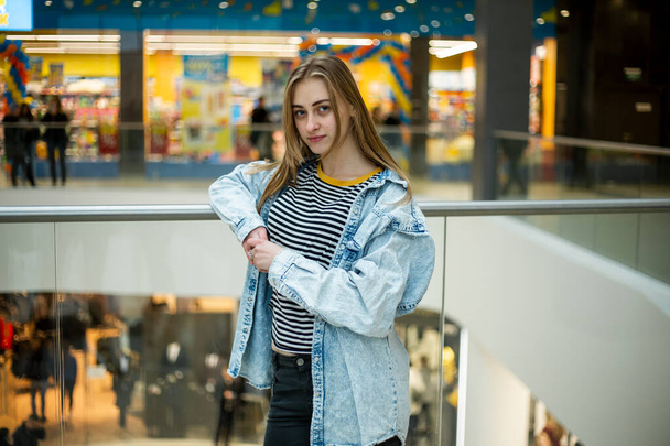 Teenager. Young pretty white caucasian teenage girl with long hair with problem skin and long hair in a shopping center near the railing. - Foto, afbeelding