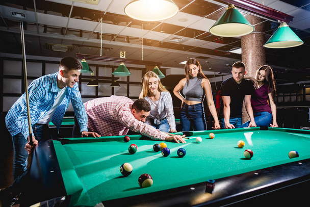 Group of young cheerful friends playing billiards. Funny time after work - 写真・画像