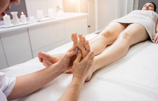 Beautiful young woman enjoying foot massage in spa salon. Cosmetology concept - Фото, зображення