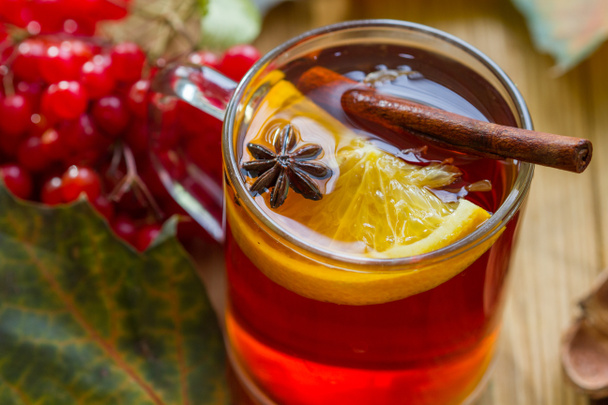 Viburnum en warme thee met sinaasappel, anijs en kaneel op een houten tafel met herfstbladeren. - Foto, afbeelding