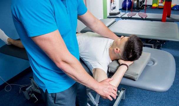 Rehabilitation therapy. Physiotherapist working with young male patient in the rehabilitation center. Treatment pain in spine - Zdjęcie, obraz