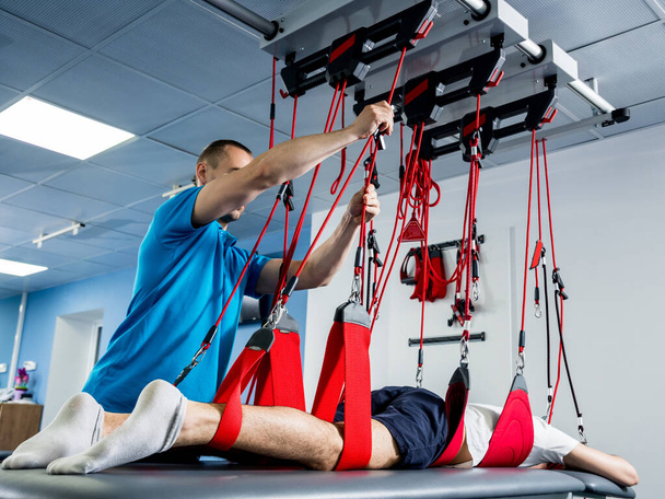 Physiotherapy. Suspension training therapy. Young man doing fitness traction therapy with suspension-based exercise training system - Foto, afbeelding