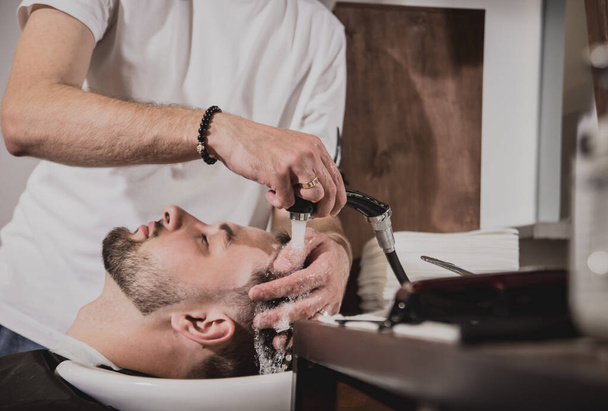 Young man with trendy haircut at barber shop. Barber washes customer head. Concept barbershop. - Foto, Bild